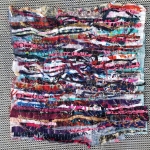 Image of strips of variously colored fabrics stitched together in a grid pattern.